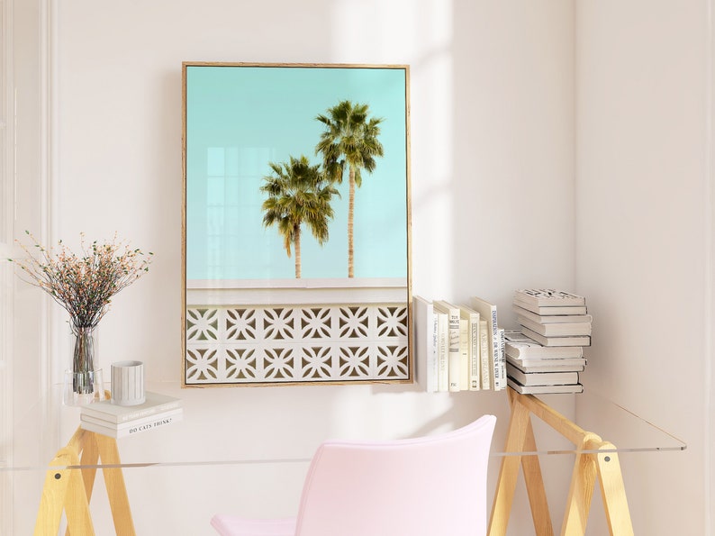 May include: A framed print of two palm trees against a light blue sky. The trees are silhouetted against a white wall with a decorative pattern.