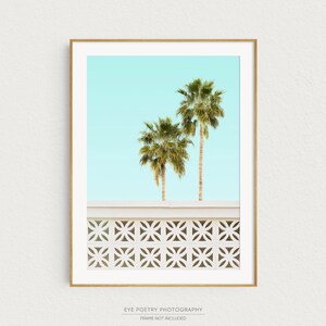 May include: A framed print of two palm trees against a light blue sky. The trees are in front of a white wall with a geometric pattern.