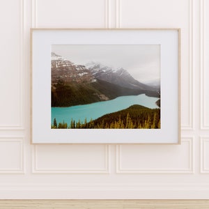 May include: A framed photograph of a mountain range with a turquoise lake in the foreground. The mountains are covered in snow and the lake is surrounded by trees.