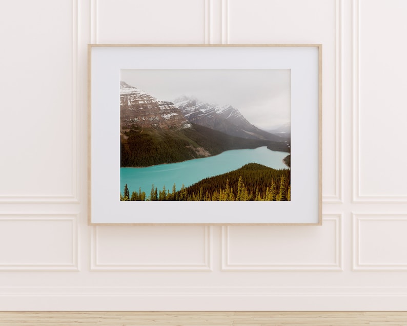 May include: A framed photograph of a mountain range with a turquoise lake in the foreground. The mountains are covered in snow and the lake is surrounded by trees.
