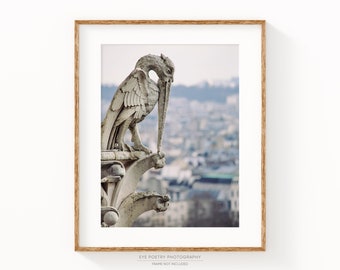 May include: A close-up of a stone gargoyle sculpture perched atop a building, with a cityscape in the background. The gargoyle has a long, pointed beak and wings, and is carved in a realistic style.