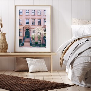 May include: A framed photograph of a row of brick townhouses with a white door and steps leading up to the entrance. The houses are decorated with blooming white flowers.