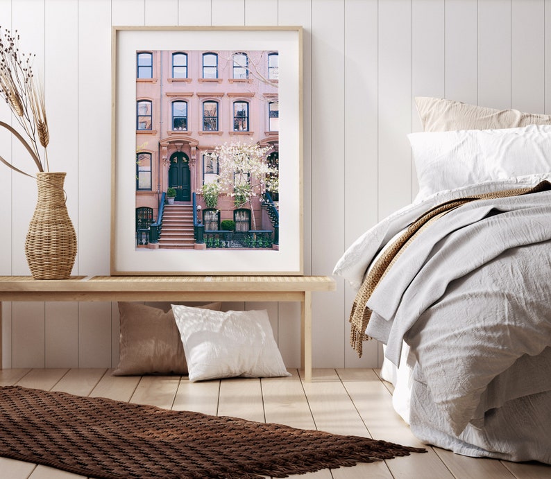 May include: A framed photograph of a row of brick townhouses with a white door and steps leading up to the entrance. The houses are decorated with blooming white flowers.