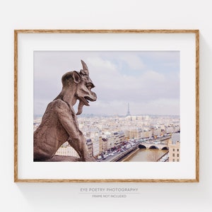 May include: A stone gargoyle sits atop a building overlooking the city of Paris, France. The Eiffel Tower is visible in the distance. The city is covered in a light dusting of snow.