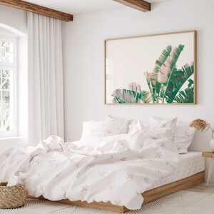 K&ouml;nnte beinhalten: Ein wei&szlig;es Bett mit einem wei&szlig;en Bettbezug und wei&szlig;en Kissenbez&uuml;gen. Der Bettbezug hat ein dezentes Sternenmuster. Das Bett ist mit einer wei&szlig;en Tagesdecke bezogen. An der Wand hinter dem Bett h&auml;ngt ein gerahmtes Bild mit tropischen Bl&auml;ttern.