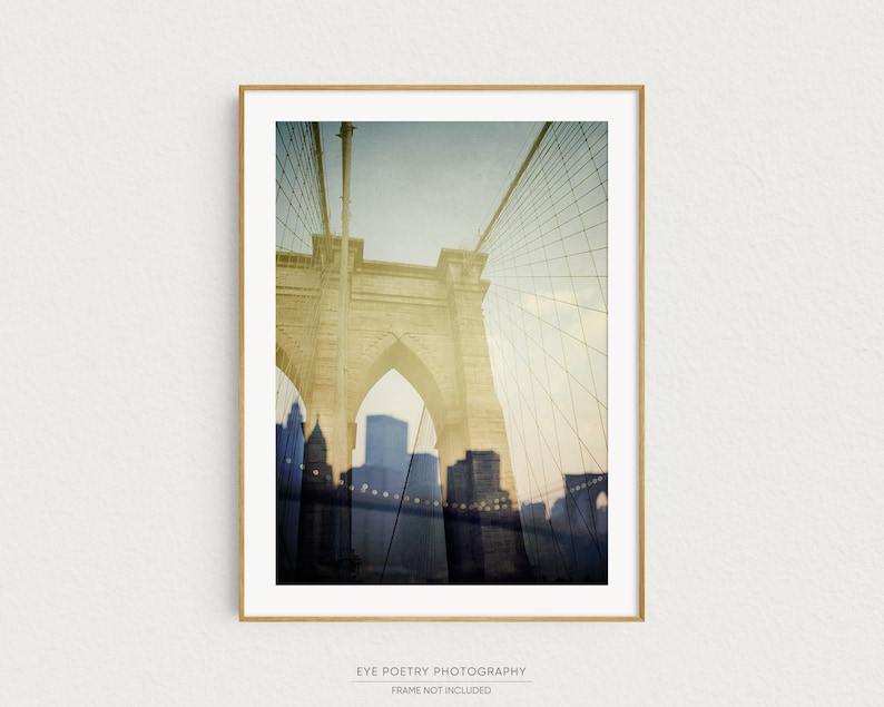 Puede incluir: Una fotograf&iacute;a de estilo vintage del puente de Brooklyn en la ciudad de Nueva York. El puente es de color amarillo claro y el fondo es de un azul brumoso con un patr&oacute;n de cuadr&iacute;cula. La imagen est&aacute; enmarcada en un marco de madera claro.