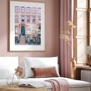May include: A framed photograph of a pink brick building with a green door and a set of stairs leading up to it. The building is surrounded by trees and flowers.
