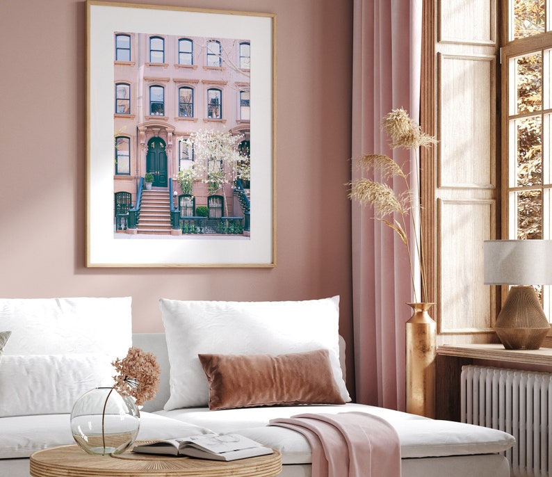 May include: A framed photograph of a pink brick building with a green door and a set of stairs leading up to it. The building is surrounded by trees and flowers.