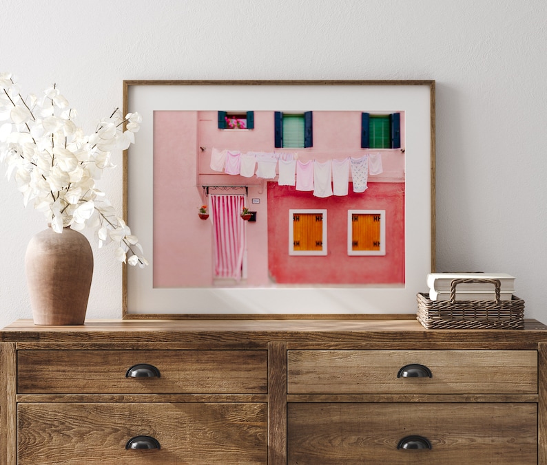 Peut inclure: Une photographie encadr&eacute;e d'un b&acirc;timent rose avec du linge blanc suspendu &agrave; une corde &agrave; linge. Le b&acirc;timent a des fen&ecirc;tres vertes et des volets orange.