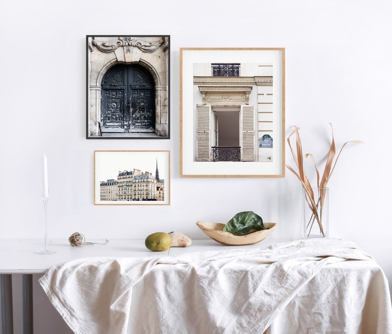 May include: Three framed black and white photographs of Parisian architecture. The top left photo shows a large, ornate doorway with a black door. The top right photo shows a white building with a doorway and a balcony. The bottom photo shows a building with multiple windows and a spire.