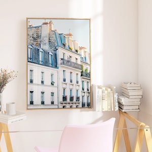 Puede incluir: Una impresi&oacute;n enmarcada de un paisaje urbano parisino con edificios blancos y acentos azules. Los edificios tienen balcones y ventanas, y el cielo es azul claro.