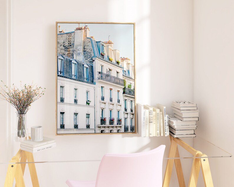 Puede incluir: Una impresi&oacute;n enmarcada de un paisaje urbano parisino con edificios blancos y acentos azules. Los edificios tienen balcones y ventanas, y el cielo es azul claro.