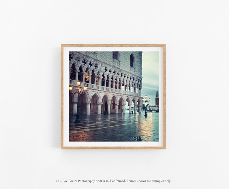 May include: A photograph of a large building with arches and columns in a square. The building is made of white stone and has a lot of detail. The square is empty and wet, and there are streetlights on either side of the building.