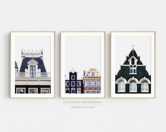 May include: Three framed prints of colorful buildings in Amsterdam, Netherlands. The prints feature a close-up of a building with a black roof and white trim, a row of buildings with black and red brick facades, and a green building with white trim and arched windows.