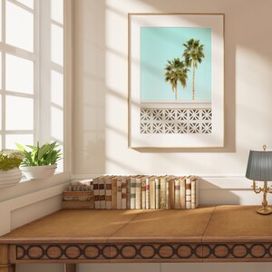 May include: A wooden desk with a decorative border, a framed print of palm trees against a blue sky, and a gold table lamp with a gray pleated shade.