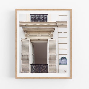May include: A white building with a window with white wooden shutters and a black wrought iron balcony. The building has a sign that reads "Rue des Martyrs".