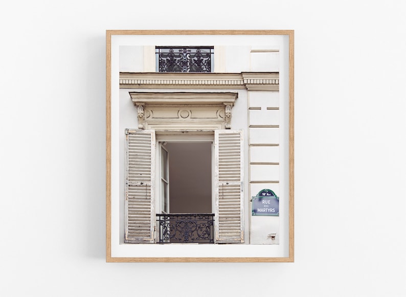 May include: A white building with a window with white wooden shutters and a black wrought iron balcony. The building has a sign that reads "Rue des Martyrs".