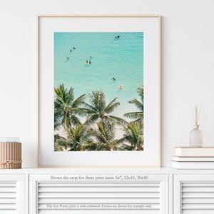 May include: An aerial view of a tropical beach with palm trees and turquoise water. People are swimming and paddleboarding in the ocean.