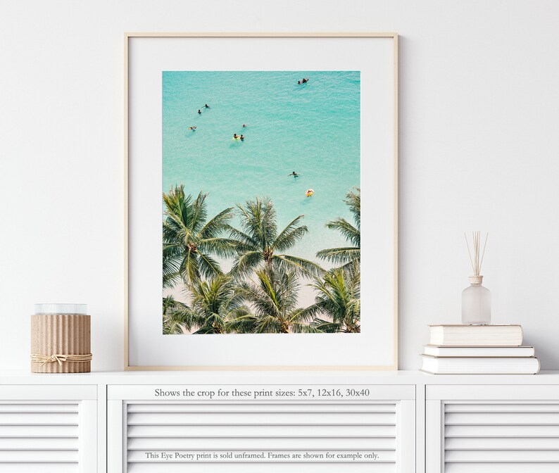 May include: An aerial view of a tropical beach with palm trees and turquoise water. People are swimming and paddleboarding in the ocean.