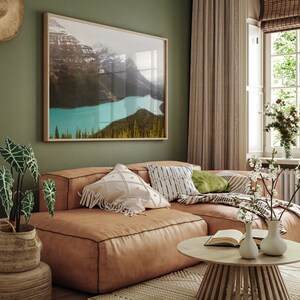 May include: A brown leather sectional sofa with white and black patterned throw pillows, a green throw pillow, and a blanket. The sofa is in a living room with a window, a green wall, and a framed picture of a mountain lake.