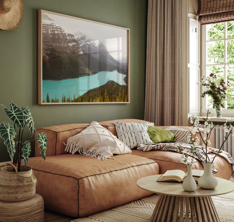 May include: A brown leather sectional sofa with white and black patterned throw pillows, a green throw pillow, and a blanket. The sofa is in a living room with a window, a green wall, and a framed picture of a mountain lake.