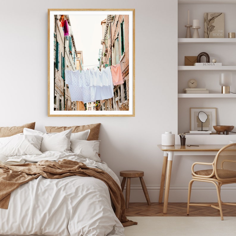 Pu&ograve; includere: Una fotografia incorniciata di una stretta via in una citt&agrave; europea con biancheria appesa a uno stendino. Gli edifici sono dipinti in tonalit&agrave; di rosa e giallo, e la biancheria &egrave; un mix di bianco e colori pastello.