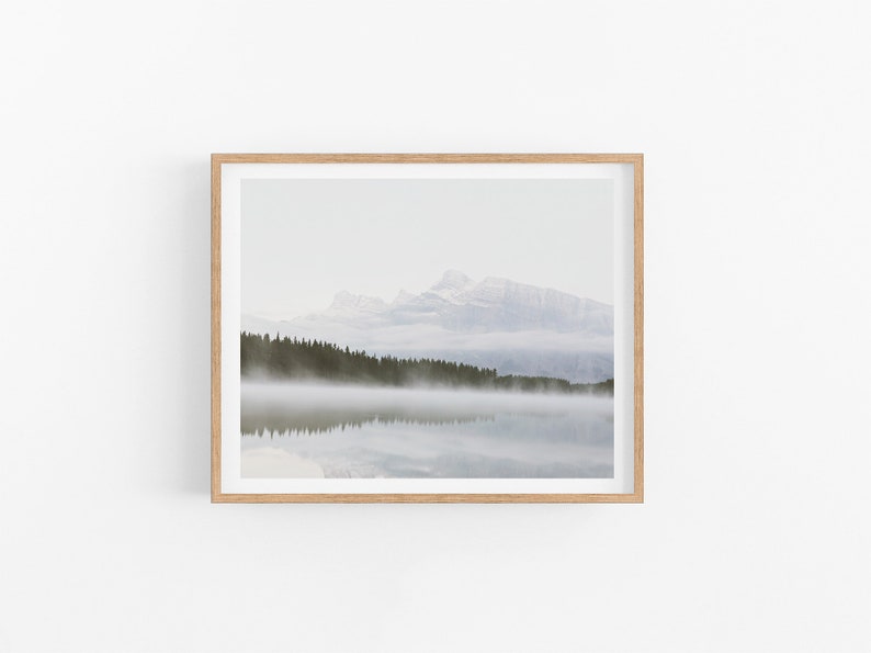 May include: A framed photograph of a mountain range reflected in a still lake with fog rolling in over a line of trees.