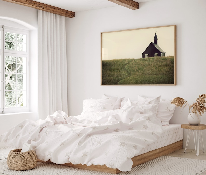 K&ouml;nnte beinhalten: Ein wei&szlig;es Bett mit einer wei&szlig;en und grauen Bettw&auml;sche mit Sternenmuster und Kissen. Das Bett steht in einem Schlafzimmer mit einem gro&szlig;en Fenster und einem gerahmten Druck einer kleinen Kirche auf einem grasbewachsenen H&uuml;gel.