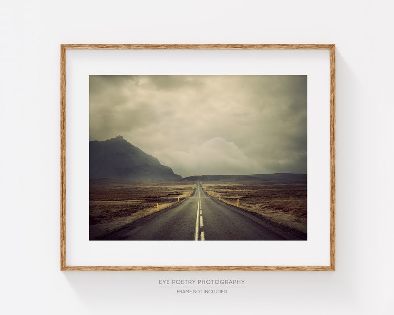 May include: A long, straight road stretches into the distance, disappearing into a cloudy sky. The road is lined with yellow lines and is surrounded by a vast, empty landscape.