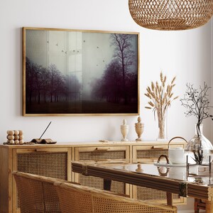 May include: A framed landscape art print depicting a misty forest scene with trees and flying birds. The artwork is displayed above a wooden cabinet with woven rattan doors. Decorative items include vases and a woven pendant light.