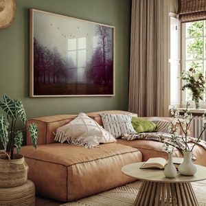 May include: A cozy living room scene featuring a large, framed landscape art piece with trees in a misty setting. A brown leather sectional sofa is adorned with decorative pillows. A round wooden coffee table and potted plants complete the inviting space.