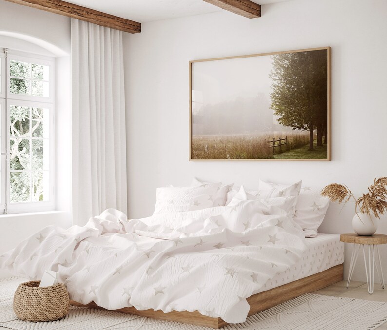 K&ouml;nnte beinhalten: Ein wei&szlig;es Bett mit einem wei&szlig;en und grauen Sternenmuster-Bettbezug und passenden Kissenbez&uuml;gen. Das Bett ist mit einem wei&szlig;en Laken und einer wei&szlig;en Decke bezogen. Das Bett steht in einem Schlafzimmer mit einem gro&szlig;en Fenster und einem gerahmten Bild eines nebligen Feldes mit einem Baum an der Wand.