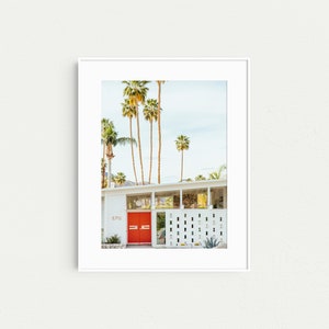 May include: A white mid-century modern house with a bright red door and a palm tree lined driveway. The house number is 1718.