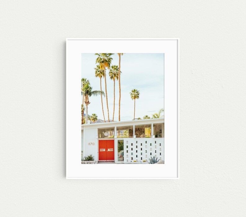 May include: A white mid-century modern house with a bright red door and a palm tree lined driveway. The house number is 1718.