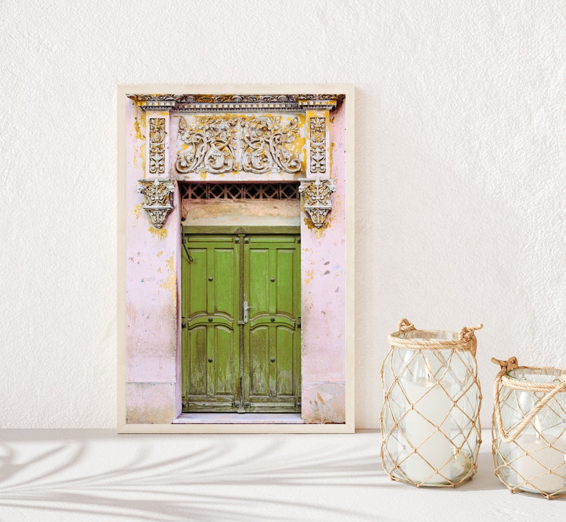 May include: A framed photograph of a green wooden door with ornate carvings above it. The door is set in a pink building with peeling paint.