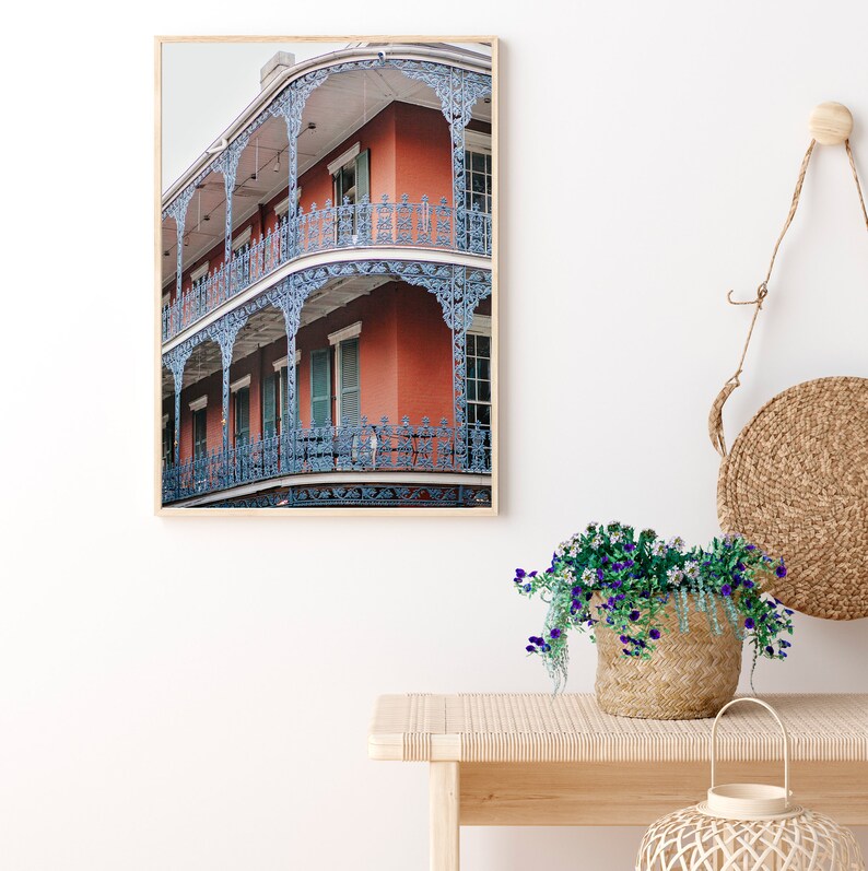 May include: A framed photograph of a red brick building with blue iron balconies and railings. The building has a vintage aesthetic and is a classic example of New Orleans architecture.