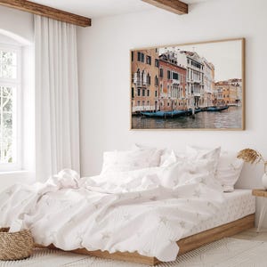May include: A white bed with a white and gray star patterned duvet cover and two white pillowcases. The bed is in a bedroom with a large window and a framed photograph of a canal in Venice, Italy.