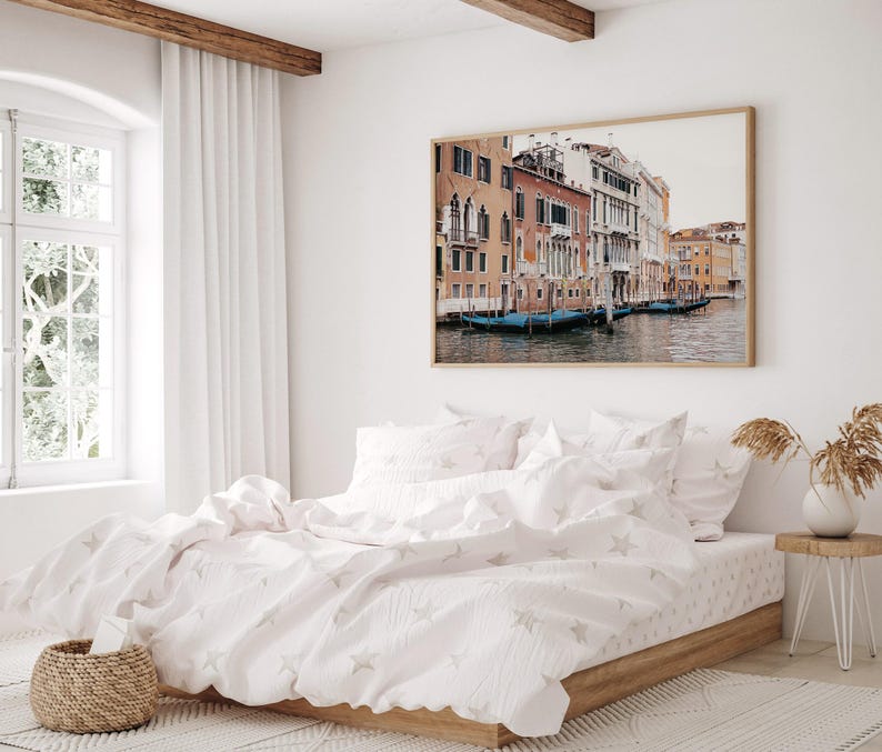 May include: A white bed with a white and gray star patterned duvet cover and two white pillowcases. The bed is in a bedroom with a large window and a framed photograph of a canal in Venice, Italy.
