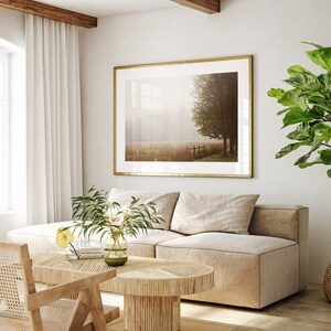K&ouml;nnte beinhalten: Ein hellbeiges Ecksofa mit zwei Kissen steht in einem Wohnzimmer mit einem gro&szlig;en gerahmten Druck einer nebligen Landschaft dar&uuml;ber. Ein kleiner Holz-Couchtisch steht vor dem Sofa, und eine Topfpflanze mit gro&szlig;en gr&uuml;nen Bl&auml;ttern steht in der Ecke des Raumes.