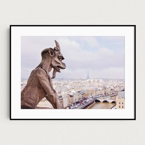 May include: A stone gargoyle sits atop a building overlooking the city of Paris, France. The Eiffel Tower is visible in the distance.