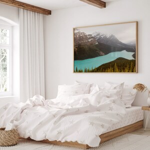 May include: A white bed with a white duvet cover and white pillowcases. The duvet cover has a subtle star pattern. The bed is in a bedroom with a large window and a framed photograph of a mountain lake.
