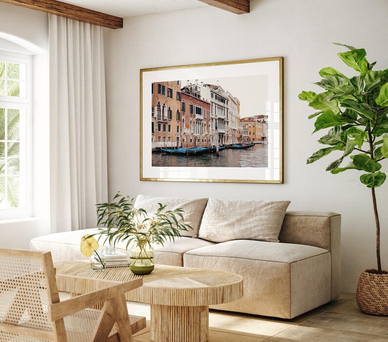 May include: A living room interior with a beige sectional sofa, a wooden coffee table, and a framed photograph of a canal in Venice, Italy. The photograph shows colorful buildings lining the canal, with gondolas floating in the water.