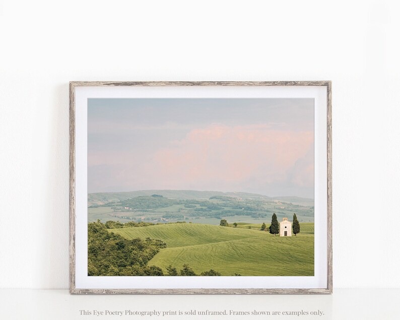 May include: A photograph of a white chapel in a field of green rolling hills. The sky is a soft pink and blue.