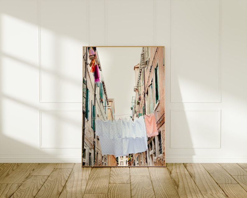 Pu&ograve; includere: Una fotografia di una stretta via in una citt&agrave; europea con biancheria colorata appesa a uno stenditoio. Gli edifici sono antichi e hanno un fascino rustico. La strada &egrave; fiancheggiata da negozi e caff&egrave;.