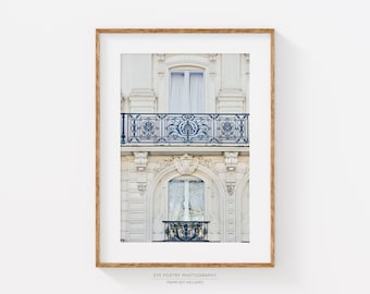May include: A photograph of a white building with two windows and a balcony. The balcony has a black wrought iron railing with intricate designs. The windows have white curtains and are framed by white trim. The building is in a European style.