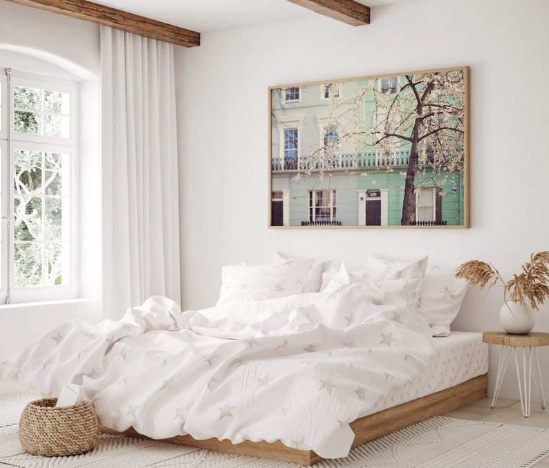 May include: A white bed with a white duvet cover and white pillowcases. The duvet cover has a subtle star pattern. The bed is in a bedroom with a window and a framed print of a building with a tree in front of it.