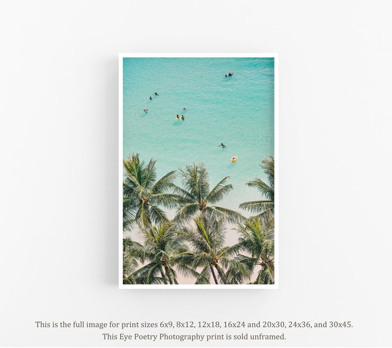 May include: An aerial view of a tropical beach with palm trees and turquoise water. People are swimming and surfing in the ocean.