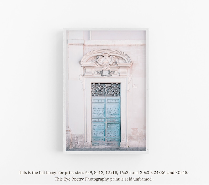 May include: A vintage, light blue door with intricate ironwork details, set within a pale pink building with ornate trim. The door is framed by a white archway.
