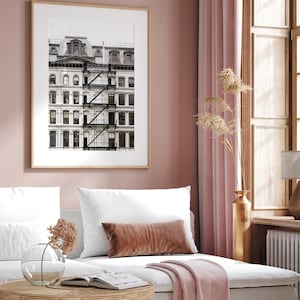 Puede incluir: Una fotograf&iacute;a en blanco y negro enmarcada de un edificio blanco con una escalera de incendios. El edificio tiene varias ventanas y est&aacute; sobre un fondo gris claro. La foto est&aacute; colgada en una pared rosa claro.