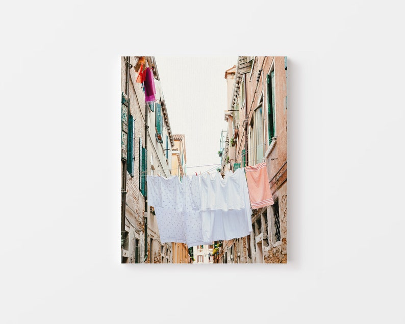 May include: A narrow alleyway in a European city with white laundry hanging on a clothesline between two buildings. The buildings are painted in shades of pink and yellow.